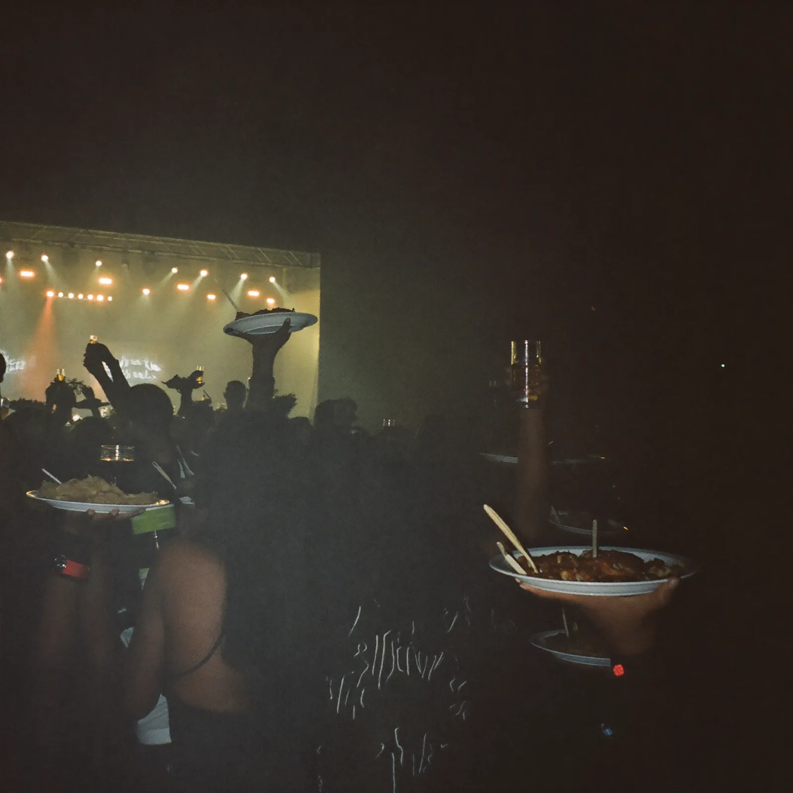 A crowd at a night food and music event under scarlet and yellow lights.